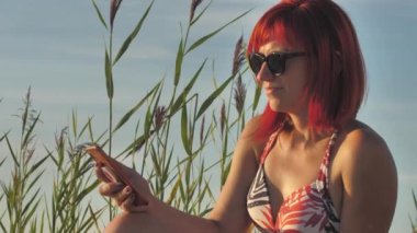 Woman with mobile phone on seashore at sunset. Beautiful woman on the beach under the hot sun