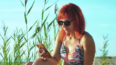 Woman with mobile phone on seashore at sunset. Beautiful woman on the beach under the hot sun