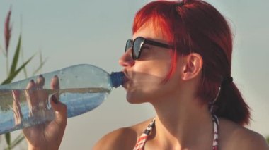 Woman with water bottle on the seashore at sunset. A woman drinks water from a bottle on the beach