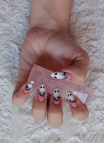 Girl with Halloween-themed nails on a fluffy white blanket holding a rose quartz point. Isolated on a white surface. White and pink nails with ghosts and eyes