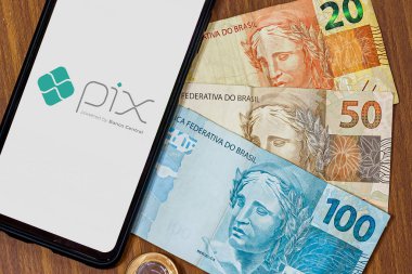 Sao Paulo, Brezilya. Pix logosu akıllı telefon ekranında ve etrafında birden fazla bozuk para var. Pix, Brezilya ve Brezilya hükümetinin yeni ödeme ve transfer sistemi..