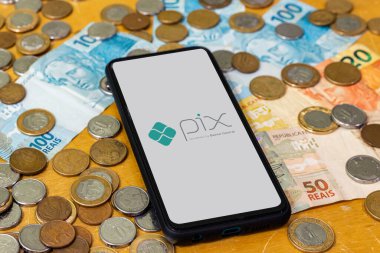 Sao Paulo, Brezilya. Pix logosu akıllı telefon ekranında ve etrafında birden fazla bozuk para var. Pix, Brezilya ve Brezilya hükümetinin yeni ödeme ve transfer sistemi..