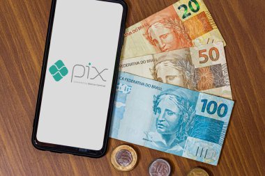 Sao Paulo, Brezilya. Pix logosu akıllı telefon ekranında ve etrafında birden fazla bozuk para var. Pix, Brezilya ve Brezilya hükümetinin yeni ödeme ve transfer sistemi..