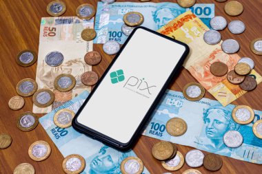 Sao Paulo, Brezilya. Pix logosu akıllı telefon ekranında ve etrafında birden fazla bozuk para var. Pix, Brezilya ve Brezilya hükümetinin yeni ödeme ve transfer sistemi..