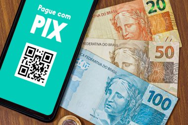 Pix akıllı telefon ekranında, etrafında birden fazla bozuk para var. Pix, Brezilya ve Brezilya hükümetinin yeni ödeme ve transfer sistemi..