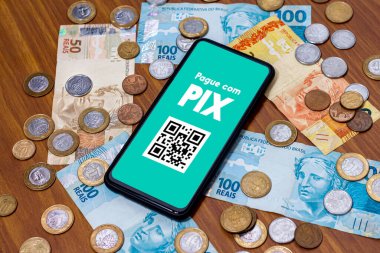 Pix akıllı telefon ekranında, etrafında birden fazla bozuk para var. Pix, Brezilya ve Brezilya hükümetinin yeni ödeme ve transfer sistemi..
