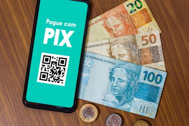 Pix akıllı telefon ekranında, etrafında birden fazla bozuk para var. Pix, Brezilya ve Brezilya hükümetinin yeni ödeme ve transfer sistemi..