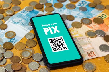 Pix akıllı telefon ekranında, etrafında birden fazla bozuk para var. Pix, Brezilya ve Brezilya hükümetinin yeni ödeme ve transfer sistemi..