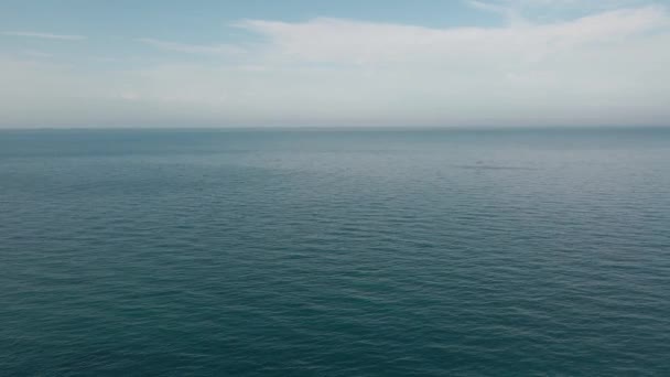 Ένα αρσενικό πεζοπόρος με σακίδιο στέκεται στην άκρη του βράχου στο μπλε του ουρανού και της θάλασσας ορίζοντα φόντο κατά τη διάρκεια αθλητικής τουριστικής δραστηριότητας αναψυχής — Αρχείο Βίντεο