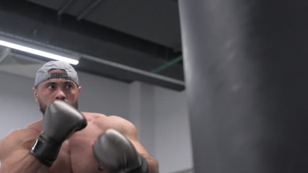Сильний молодий чоловік з бородою носить капсульну сумку в боксерських рукавичках під час тренування в приміщенні спортивної діяльності з використанням рук і ніг у повільному русі — стокове відео