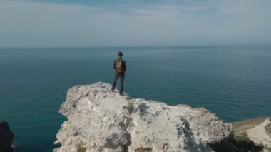 Yavaş hava rotasyonu drone görüntüsü aktif yürüyüş adam sırt çantalı kayalık bir dağ üzerinde duruyor açık hava eğlence eğlence seyahat etkinlik meditasyon ilham sırasında gökyüzü ufuk ile