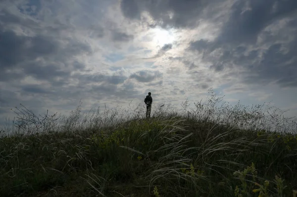Έννοια μοναξιά του ταξιδιού ενεργό μοναχικός άνθρωπος στο λόφο γρασίδι με συννεφιασμένο ηλιοβασίλεμα στο παρασκήνιο με αντίγραφο χώρου κατά τη διάρκεια ταξιδιού περιπέτεια — Φωτογραφία Αρχείου