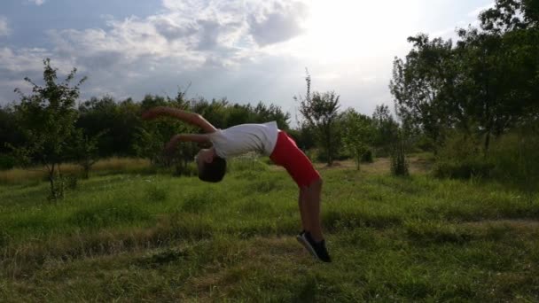 Aktiv liten frisk unge i vit jersey och röda shorts gör slow motion somesault tillbaka flip utomhus natur park fritid aktivitet — Stockvideo
