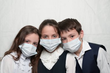 Coronavirus COVID-19 epidemi karantinası sırasında tıbbi maskeli ve okul üniformalı üç küçük çocuk.