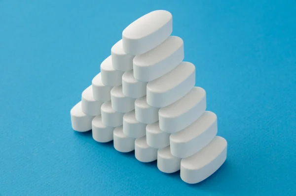 Molte compresse bianche farmacologiche pillole di farmaci su sfondo blu con spazio di copia Fotografia Stock
