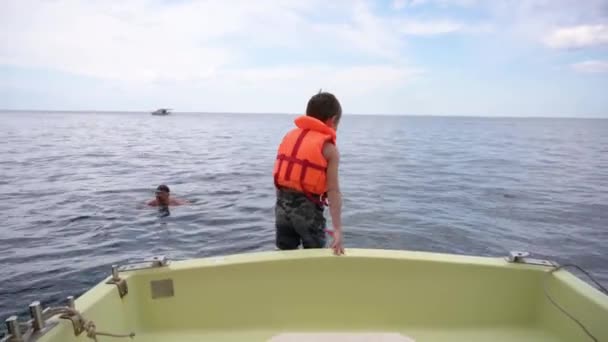 Kleines aktives Kind in orangefarbener Schwimmweste springt im Sommer während einer Seekreuzfahrt zu seinem Vater ins Wasser — Stockvideo