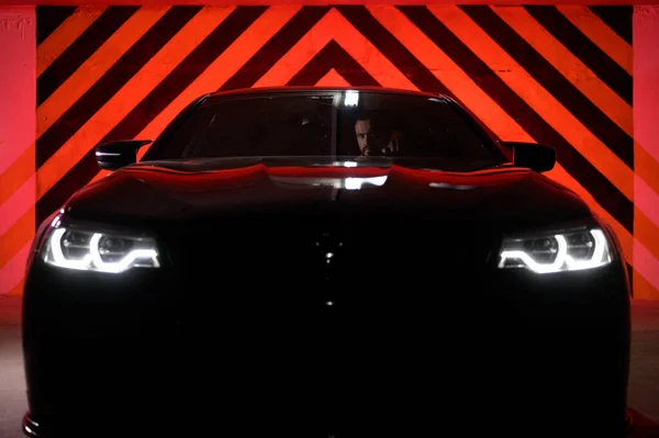 Sport muscle car with bearded male inside in undeground night city garage with with red light ready to drive Imagini stoc fără drepturi de autor