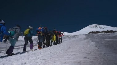 Kar dağlarında yürüyen bir grup aktif sporcu mavi gökyüzü ve üzerlerinde kopya alanı var.
