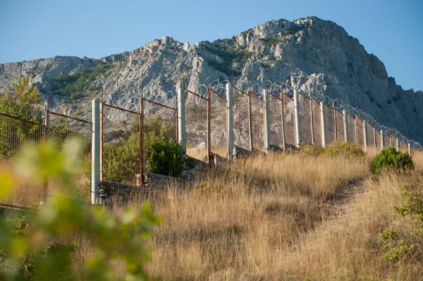 Alta recinzione per gli immigrati clandestini filo spinato rasoio al confine di stato USA Messico in montagne rocciose Immagine Stock