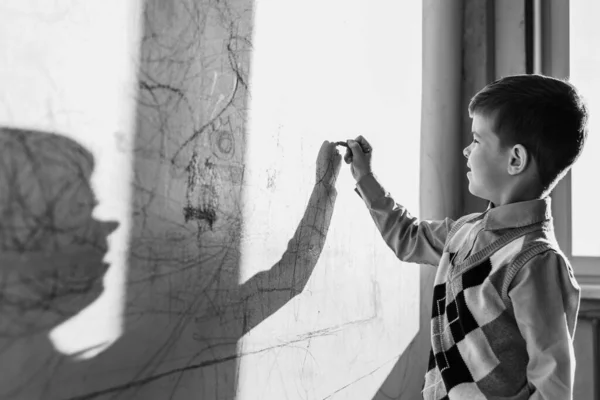 The child draws on the wall with colored chalk. The boy is engaged in creativity at home. Black and white photo
