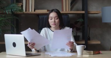Stresli motivasyonsuz Asyalı kadın belgelerde yanlışlıkla kafası karışmış, kağıtlara bakıyor, dizüstü bilgisayarla kaşlarını çatıyor, acil görevlerde başarısız oluyor, yorgunluktan ve uykusuzluktan teslim tarihini kaçırıyor.