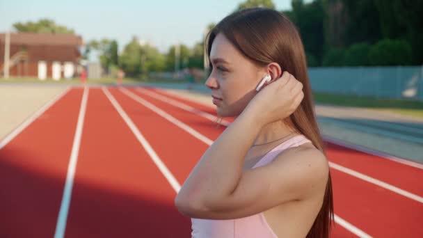 Femme coureuse proche debout avec téléphone dans les écouteurs au stade. Athlète féminine utilisant le téléphone sur la bonne voie — Video