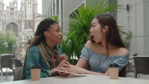 Twee multiraciale tienermeisjes die in een café zitten en tabletcomputer gebruiken. Goed nieuws, toelating tot de universiteit. Afstandsonderwijs en nieuwe leertechnologie. — Stockvideo