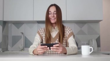 Şık baskılı yelek giymiş genç bir kadın telefonla oynarken eğleniyor. Stok görüntüleri. Şık, genç bir kadın, eğlenceli ve akıllı telefonunda hevesle oyun oynuyor. Kazanan konsept.