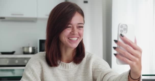 Piękne pewność siebie pozytywna dorosła kobieta w swetrze siedzi w przytulnej kanapie i rozmawia na rozmowy wideo za pomocą smartfona w domu. — Wideo stockowe