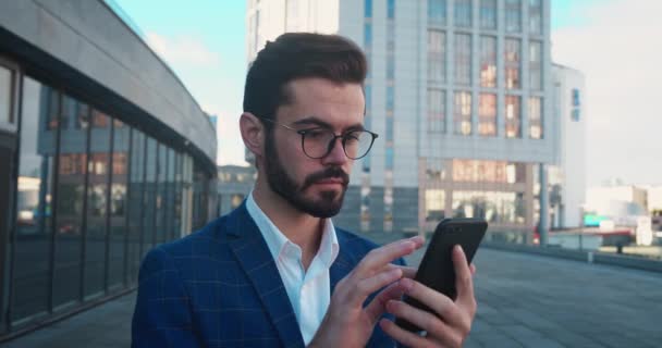 Verbazingwekkende man met een baard die naar een smartphone kijkt en WOW zegt. Aangenaam verrast jong mannetje op de stedelijke stedelijke achtergrond — Stockvideo