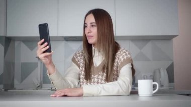 Evde akıllı telefondan görüntülü konuşma yapan genç bir kadın.