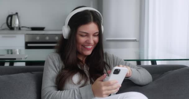 Entspannte junge Frau, die mit dem Smartphone in den sozialen Medien surft, Nachrichten checkt, Handyspiele spielt oder auf dem Sofa sitzend SMS schreibt. Millennial-Mädchen verbringt Zeit zu Hause mit Handy-Gadget-Technologie — Stockvideo
