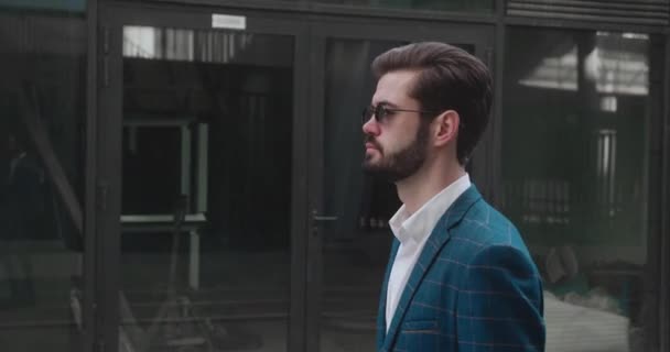 Bearded man in a Suit and with wearing dark glasses walking along business district. He confident and Looks Successful. side view. — стоковое видео