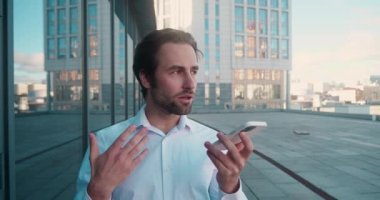 Gülümseyen genç adam hoparlörden ses tanıma mesajı kaydediyor. İş adamı sanal asistan uygulaması kullanıyor. Dahili ofisteki akıllı telefondan anımsatıyor. Dijital ai mobil yardım teknolojisi kavramı.