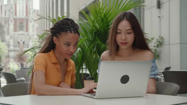 Primer plano. grupo de 2 personas. dos compañeros de estudios están trabajando en una computadora portátil, chicas asiáticas y estudiantes afroamericanos — Vídeos de Stock