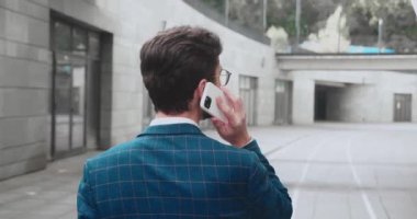 Ofis merkezinde caddede yürüyen ve telefonla konuşan, gözlüklü beyaz iş adamının arkası. Kapatın. Arka taraf. Dışarı çıkın. Kavram: yeni bir iş, iletişim, bağlantılar, bir