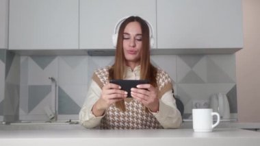Modern mutfak arka planında akıllı telefonu olan kulaklıklı bir kadın..
