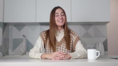 Gülümseyen genç yetişkin kadın vlogger kamera konuşmasına bak canlı video konferansı yap blog blogu kaydını evdeki modern mutfak arka planında sandalyeye oturt.