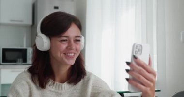 Güzel, gülümseyen esmer bir kadın beyaz koltukta otururken görüntülü sohbet eden biriyle konuşuyor..