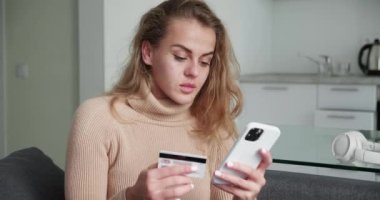 Evde cep telefonu ödemelerini kullanarak kredi kartı tutan mutlu genç bir kadın. Gülümseyen güzel müşteri müşterisi akıllı telefondan para çekme konseptini satın alıyor. E-bankacılık uygulama servisi.