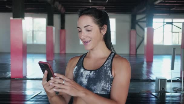 Woman have video call with smart phone in gym. Woman using mobile phone while resting during fitness training. — Video Stock