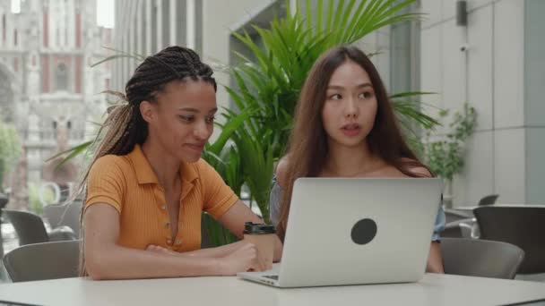Primer plano. grupo de 2 personas sentadas en la cafetería. Dos compañeros de estudios están trabajando en una computadora portátil, chicas asiáticas y estudiantes afroamericanos. — Vídeos de Stock