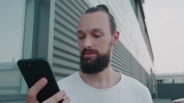 Mężczyzna millenium hipster trzyma nowoczesną wiadomość SMS-ową smartfona. Młody biznesmen wykorzystujący pomocne aplikacje mobilne do koncepcji organizacji zarządzania czasem pracy na parkingu. — Wideo stockowe