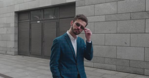 Blanke zakenman in een pak en met een donkere bril lopend op een straat in het centrum. Hij lacht en ziet er succesvol uit. — Stockvideo