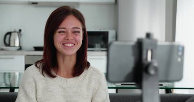 Oturma odasında tek başına oturan akıllı telefonu kullanarak video bloğu kaydeden kadın video bloğuna cihaz takan yeni video bloğu çevrimiçi canlı yayın yapan Webinar uzak sohbet, modern teknoloji video etkinliği