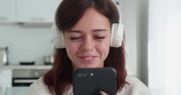 Een mooie glimlachende brunette vrouw is praten met iemand met een video chat terwijl zitten in de witte gezellige bank. — Stockvideo