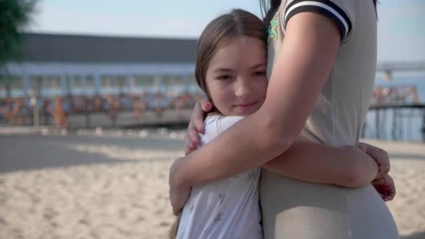 Retrato de mãe e filha feliz 9 anos de pé abraçando contra o pano de fundo perto da praia à luz do sol e sorrindo para a câmera desfrutando de momento — Vídeo de Stock