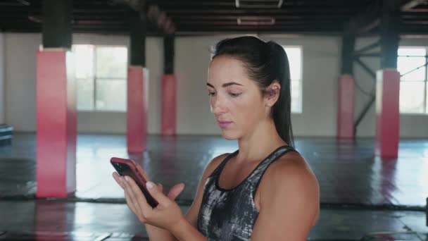Женщина с помощью смартфона с персональным тренером тренировки приложение в тренажерном зале. Женщина готовится к тренировке с помощью фитнес app.Woman с помощью мобильного телефона во время отдыха во время фитнес-тренировки. — стоковое видео