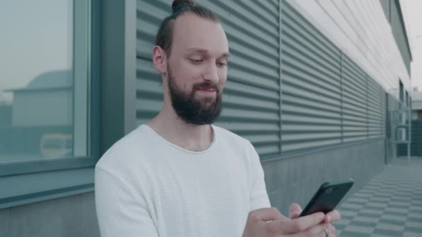 Ung skægget hipster millennial ser på skærmen smartphone og beslutter at købe online eller flips gennem nyhederne feed. – Stock-video