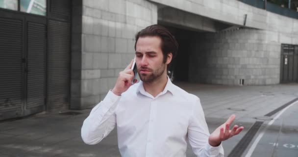 Όμορφος γενειοφόρος επιχειρηματίας με λευκό πουκάμισο που μιλάει στο τηλέφωνο περπατώντας στο δρόμο για να εργαστεί στο γραφείο. Χαρούμενο αρσενικό σε καλή διάθεση σε εξωτερικούς χώρους. — Αρχείο Βίντεο